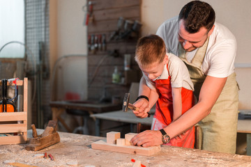 Father teaching his son the craft of carpentry in the home workshop with a hammer hammering nails...