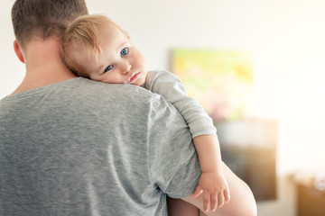 Close-up portrait of cute adorable blond caucasian toddler boy on fathers shoulder indoors. Sweet little child feeling safety on daddys hand. Responsibility and childcare. happy childhood