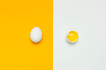 Creative food minimalistic background, Easter. White chicken egg and one broken egg with yolk on yellow gray background top view flat lay copy space. Natural healthy food, organic farming concept.
