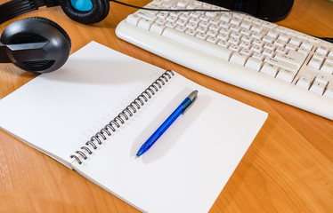notebook with pen, keyboard and headphones on the table
