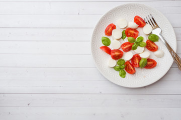 Caprese salad of tomatoes, mozzarella cheese and Basil on a white plate. Italian cuisine. Copy space