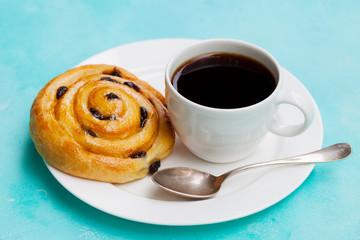 Fresh danish pastry with raisins and cup of black coffee on blue background. Close up.