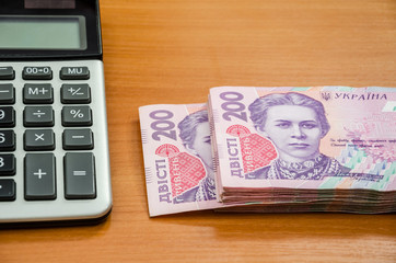 200 hryvnia and a calculator on a wooden table. Close-up.