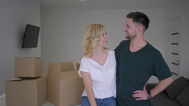 portrait of happy couple new home owners show keys to flat and hug while relocation on background of cardboard boxes