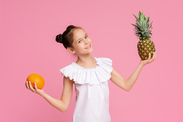 Attractive little girl holding orange and pineapple