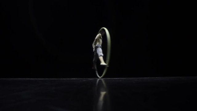 Circus performer artist in a Cyr Wheel in theatre on a black background