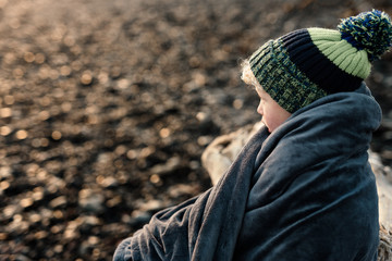 Small child wrapped in a blanket wearing a winter hat sitting outside