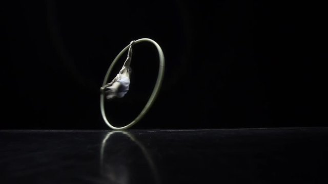 Circus performer artist in a Cyr Wheel in theatre on a black background