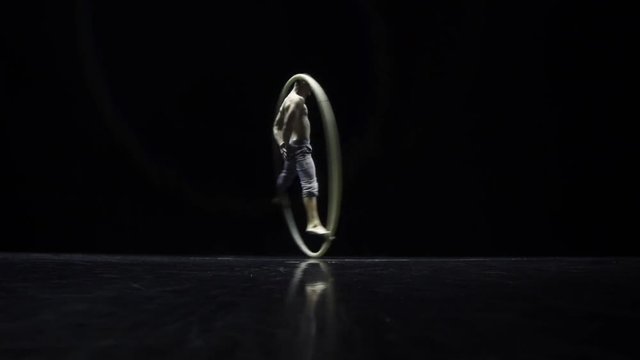 Muscular circus artist in the Cyr Wheel doing difficult tricks slow motion