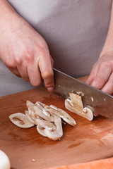 Fototapeta na wymiar young woman slicing mushrooms in a gray apron