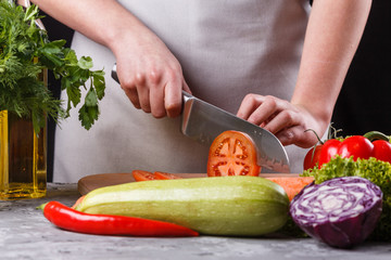 young woman slicing a tomato in a gray apron