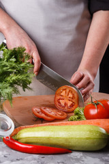 young woman slicing a tomato in a gray apron