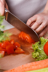 young woman slicing a tomato in a gray apron