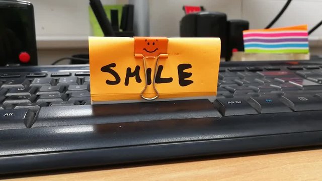 Zoom out shot, as hit Enter button in a friendly, stress-free office work environment, smiley sign on a sticky note