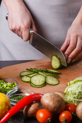 young woman in a gray apron cuts a cucumber