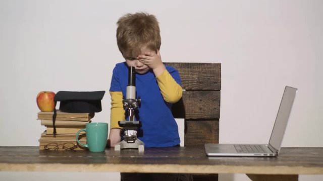 Kid boy looks in microscope. Wunderkind concept - smart small boy, scientist child working with microscope, laptop. Primary school concept. First interested in studying, learning, education. Science.