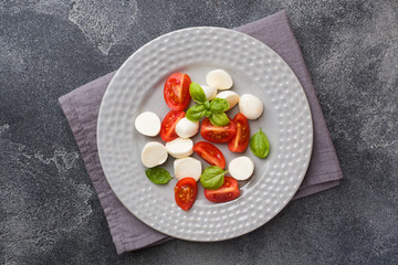 Caprese salad of tomatoes, mozzarella cheese and Basil on a dark background. Italian cuisine. Copy space