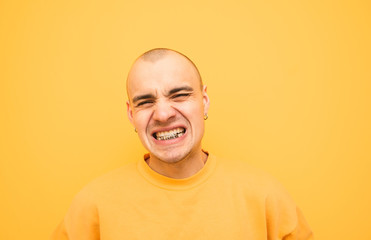 Expressive young man with a grillz on his teeth is angry with a yellow background wearing yellow...