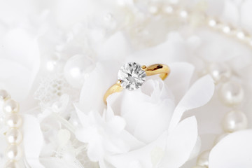 golden engagement ring with diamond on white bridal flowers background