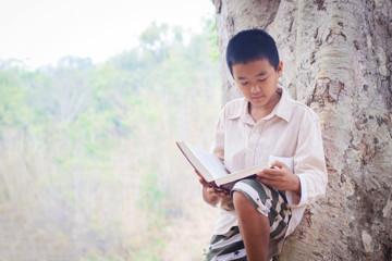 Boy asian reading his book under a tree in a autumn background.