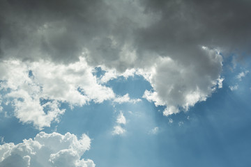 View of the sky of blue color and gray clouds through which the sun's rays make their way