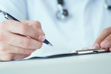 Male physician medicine doctor or pharmacist writing prescription on special form sitting at worktable. Medical care, pharmacy or health insurance concept.