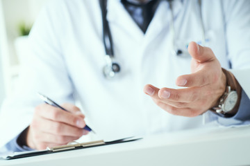 Male doctor making welcome gesture, politely inviting patient to sit down in medical office.