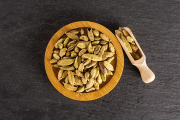 Lot of whole true cardamom pod on bamboo plate with wooden scoop flatlay on grey stone