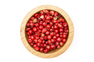 Lot of whole peruvian pink pepper in a wooden bowl flatlay isolated on white background