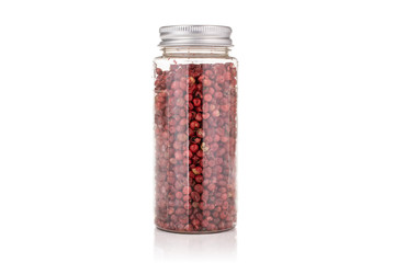 Lot of whole peruvian pink pepper in a plastic bottle isolated on white background