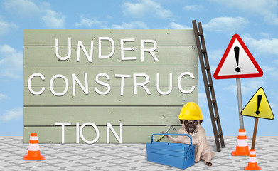 cute repairman pug puppy dog with yellow safety helmet, sitting down next to wooden board sign, with text under construction