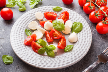 Caprese salad of tomatoes, mozzarella cheese and Basil on a dark background. Italian cuisine.