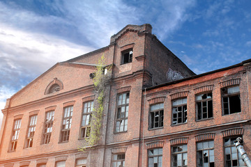 Abandoned multi-storey red brick house with broken windows against a blue sky