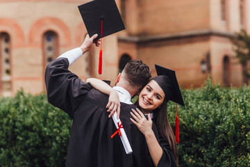 Young female graduate hugging her friend at graduation ceremony with certificate on hands!