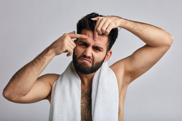 shirtless man popping a pimple. close up photo. unhappy sad man with fingers on his forehead