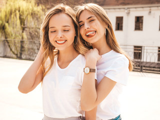 Portrait of two young beautiful blond smiling hipster girls in trendy summer white t-shirt clothes. Sexy carefree women posing on street background. Positive models having fun.Hugging