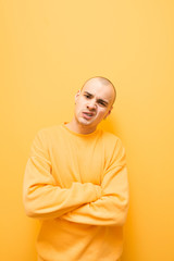 Obraz premium Portrait of a charismatic guy in bright clothes makes an aggressive face on a yellow background and looks into the camera. Evil stylish guy with grillz on his teeth poses to the camera.Isolated