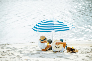 Senior couple sitting together under umbrella on the sandy beach, enjoying their retirement near the sea, rear view