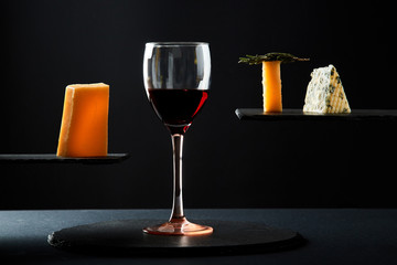 Red wine in crystal glass beside pieces of cheese on black background