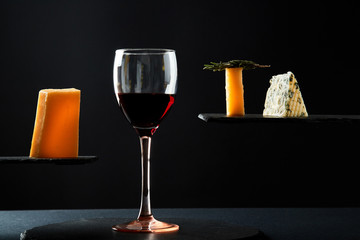 Red wine in crystal glass beside pieces of cheese on black background