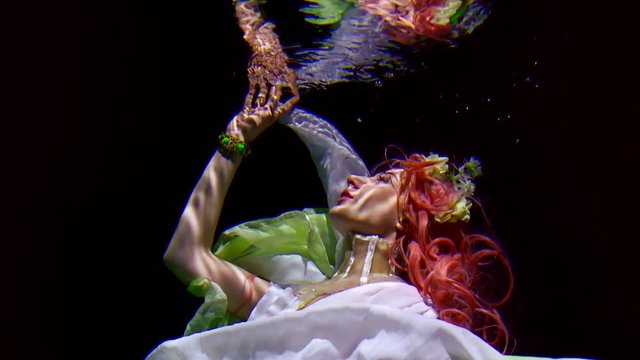 Slow motion underwater. a young mermaid woman in a dress and pink hair like in a fairy tale. looks at reflection in water as in a mirror