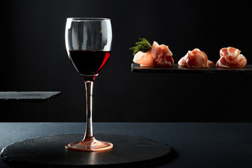 Composition of red wine in glass and pieces of meat snack on black background