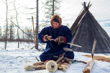 Residents of the far north,  the pasture of Nenets people, the dwelling of the peoples of the north of Yamal, a man makes wooden sleds by hand with a knife and an ax © evgenii