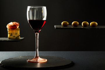 Composition of red wine in glass and pieces of prosciutto and cheese and olives on black background