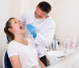 Dentist is treating young female patient which is sitting in dental chair