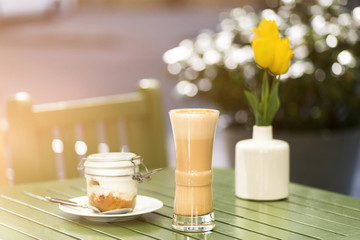 Latte coffee with cake in jar on the table in the street, terrace, outdoor cafe, sunset, outdoors . Free space for text