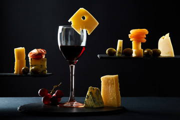 Glass of tasty red wine among assorted traditional appetizers on black background