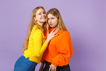 Two smiling perplexed young blonde twins sisters girls in vivid colorful clothes looking camera isolated on pastel violet blue wall background. People family lifestyle concept. Mock up copy space.