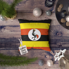 Happy New Year tag with Uganda flag on pillow. Christmas decoration concept on wooden table with lovely objects.