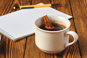 A bunch of cinnamon knitted with a rope, a cup of coffee and a notebook for writing on a wooden background close-up.